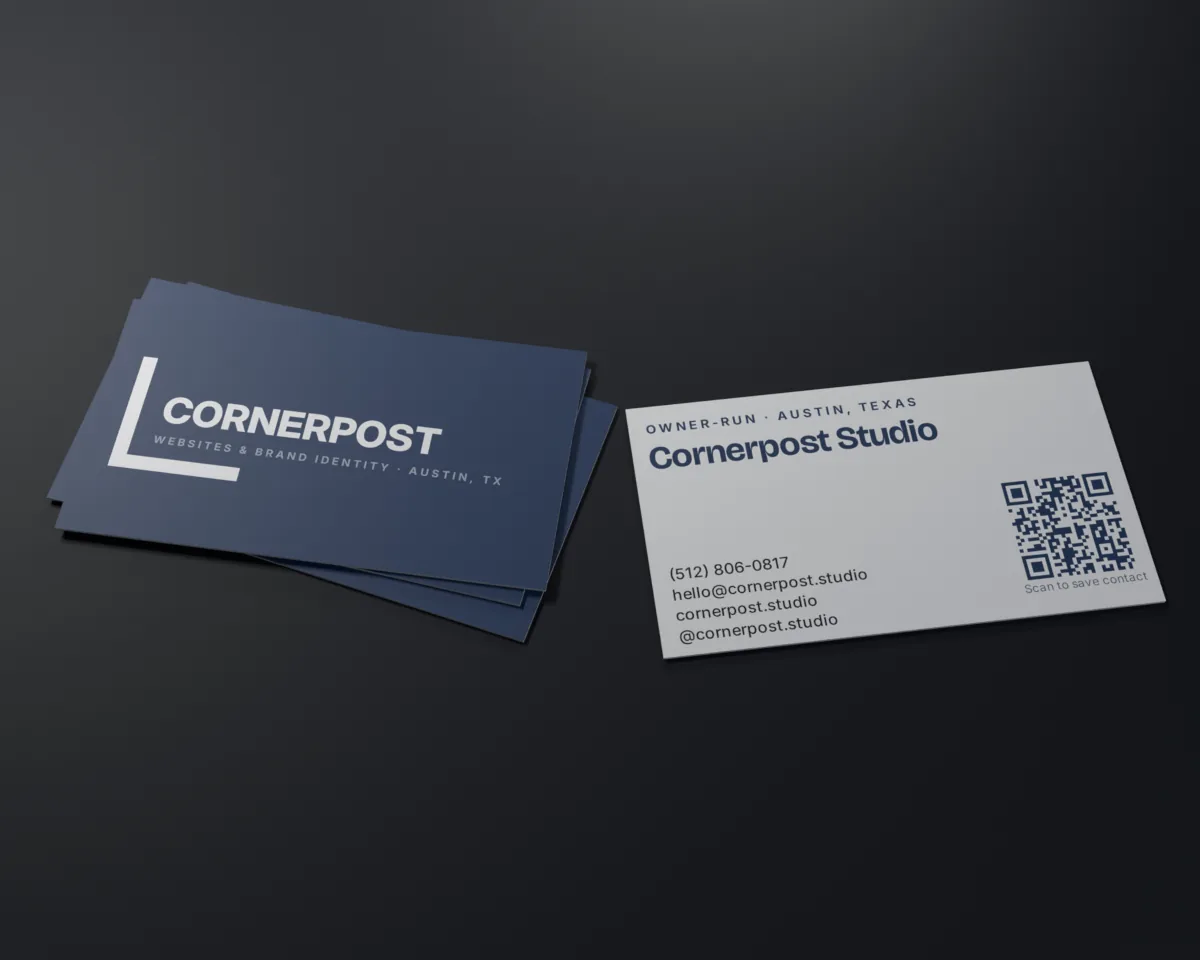 Two Cornerpost business cards on a table: the navy front with the corner bracket and wordmark, and the white back with the studio's details and a QR code.
